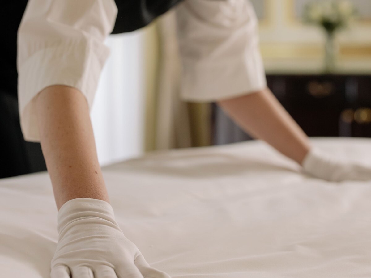 Reinigungskraft mit Handschuhen zieht das frische Laken auf einem Bett glatt