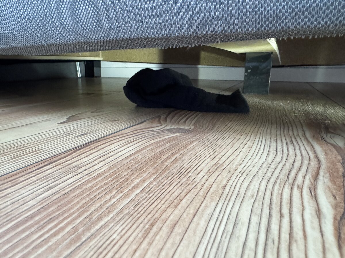 Schwarze Socke auf dem Boden unter einem Bett, entdeckt bei der Kontrolle nach der Reinigung