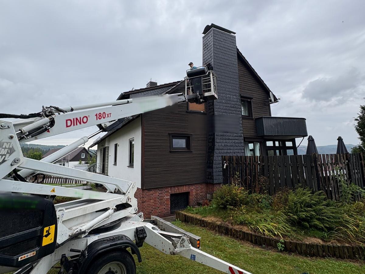 Anhänger-Arbeitsbühne vor einem Wohnhaus, der Korb steht am Giebel in Höhe des Obergeschosses
