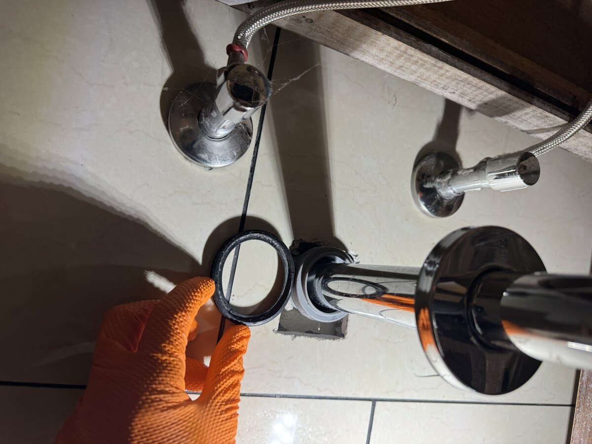 Hand im Arbeitshandschuh setzt einen Dichtring am Siphon unter einem Waschtisch ein